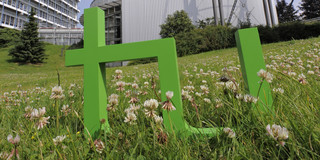 Bild des Logos der TU Dortmund platziert auf einer Wiese zwischen Gebäuden der Universität.